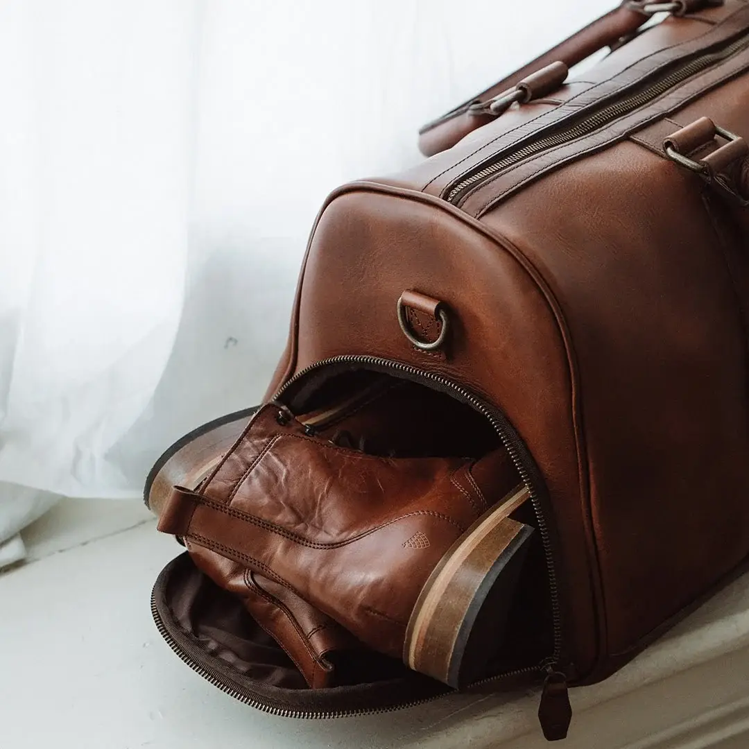 Weathered full-grain leather duffle bag resting on stone outdoors