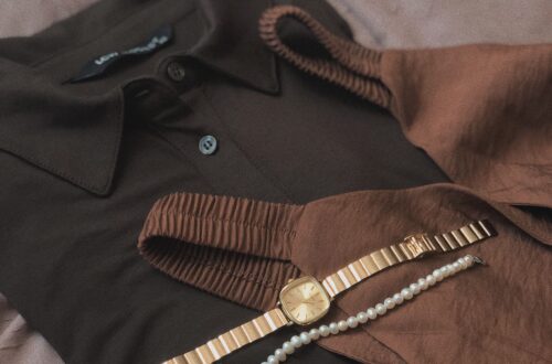 Warm neutral flat lay of a gold watch and pearl necklace draped over a soft brown knit sweater
