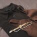 Warm neutral flat lay of a gold watch and pearl necklace draped over a soft brown knit sweater