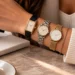 Three women's watches worn together on one wrist: a rectangular gold watch on a black strap, a steel bracelet watch and a gold mesh watch
